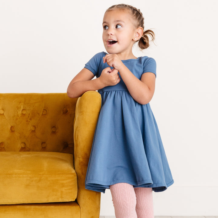 girl in denim blue twirl dress and blush pink tights with yellow velvet chair