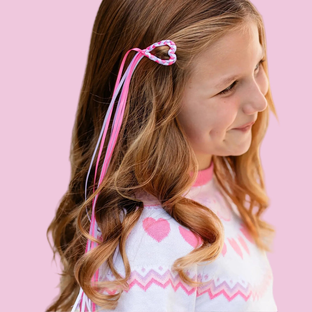 closeup of heart shaped barrette with braided ribbon in pink, white and lavender with streamer ribbon tail on young girl wearing white valentine's fair isle sweater