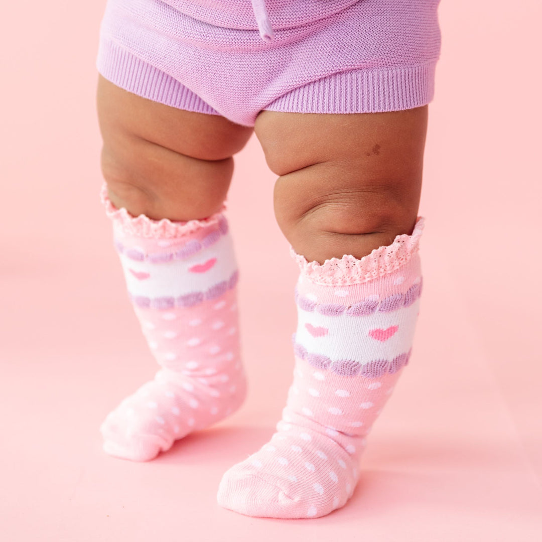 baby in pink ruffle knee highs with white dots and heart details paired with matching knit bloomers in lavender