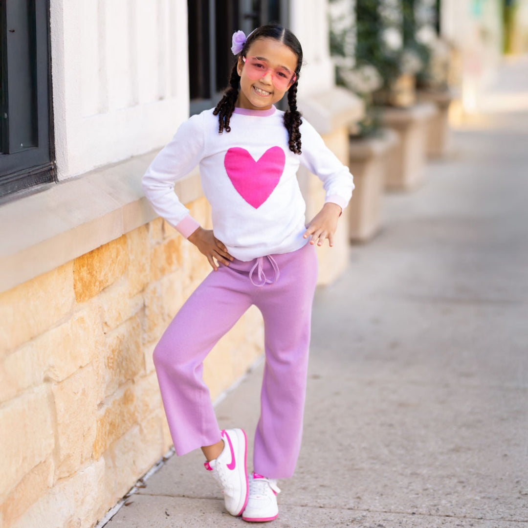 little girl posing in white cotton knit sweater with pink heart design and lavender neckline paired with matching lavender sweater pants