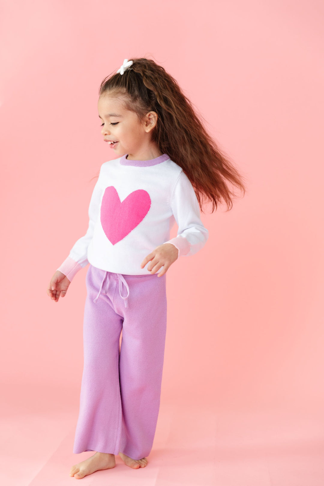 little girl in cotton knit lavender sweater pants with drawstring waistband and matching white pullover sweater with pink heart design and lavender neckline