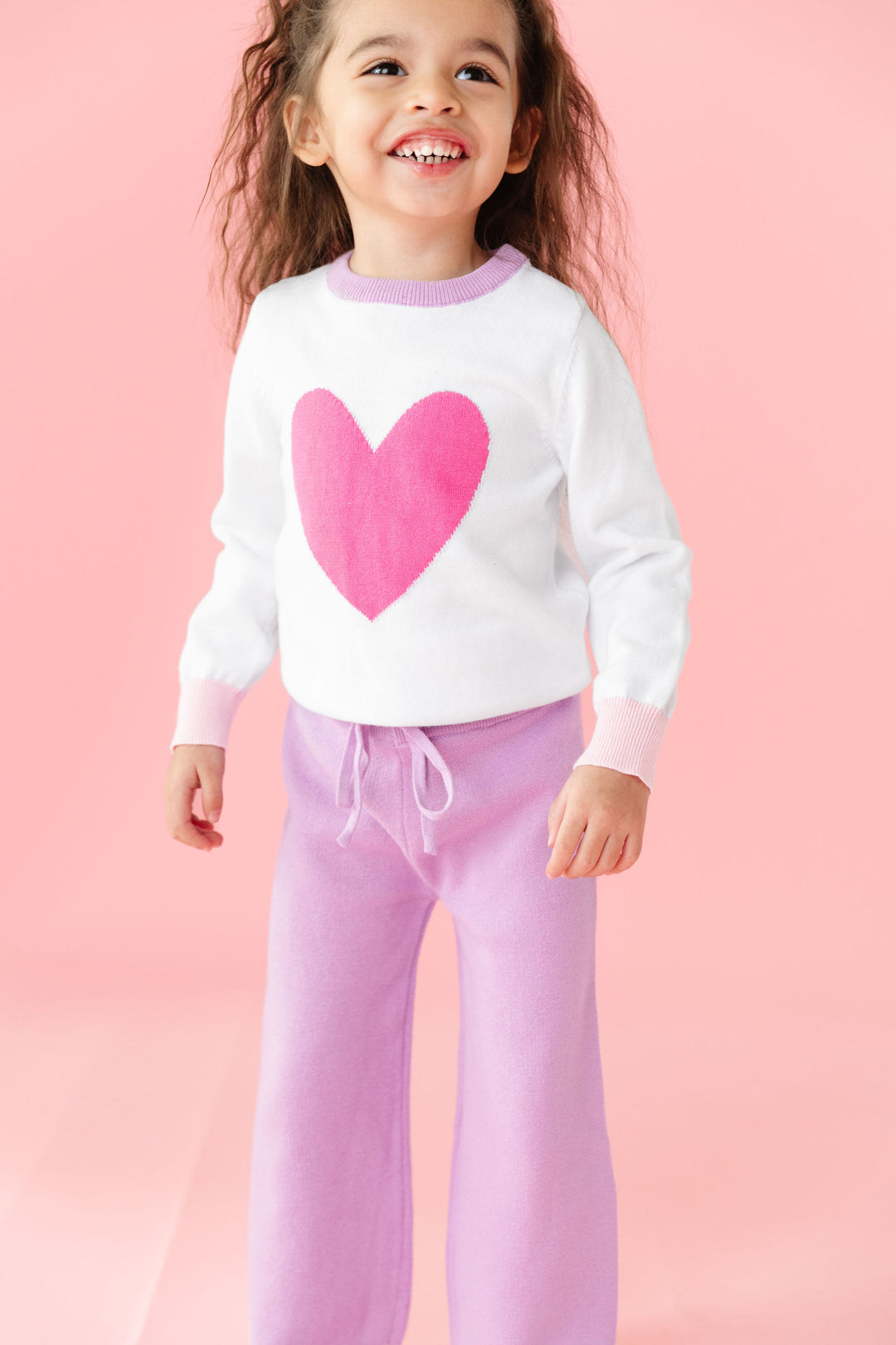 little girl in white cotton knit pullover sweater with pink heart design and matching lavender sweater pants