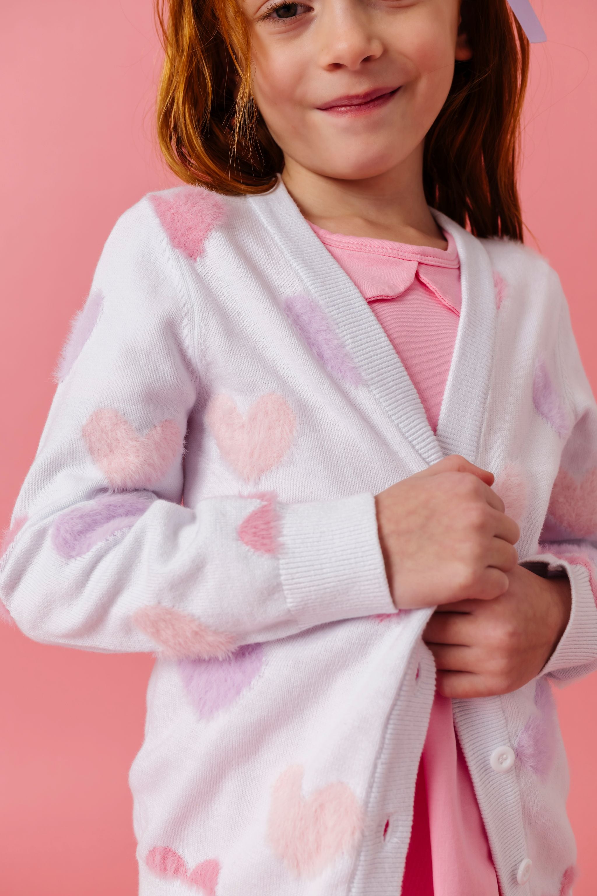 closeup of white cotton knit v-neck cardigan with pastel fuzzy hearts paired with light pink collared twirl dress for valentines day