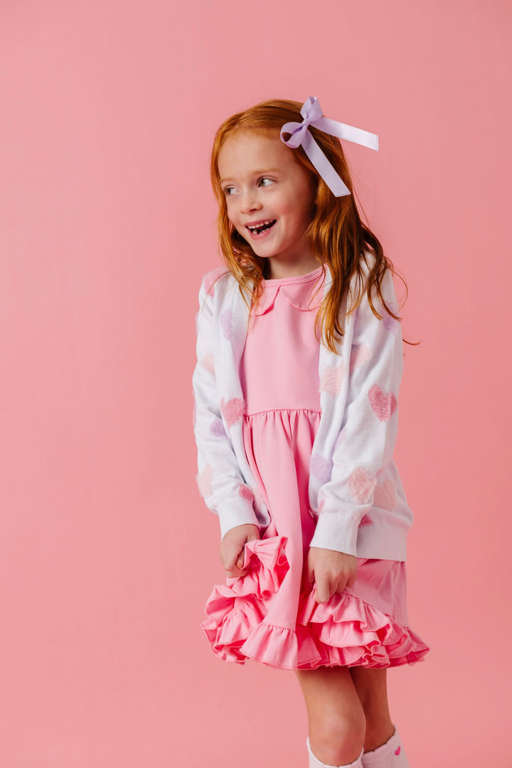 young girl in light pink collared twirl dress and white with pastel fuzzy heart cardigan, lavender ribbon hair bow and matching heart socks