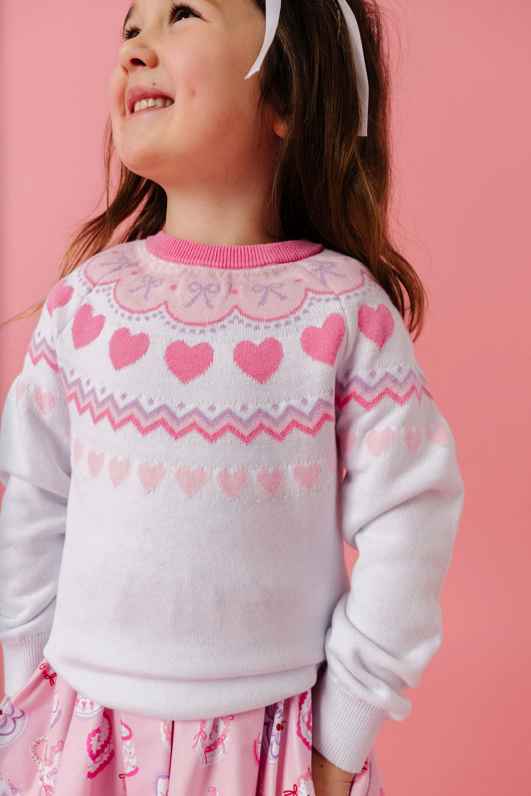 girl in white knit sweater with pink hearts and lavender bow design for Valentine's day