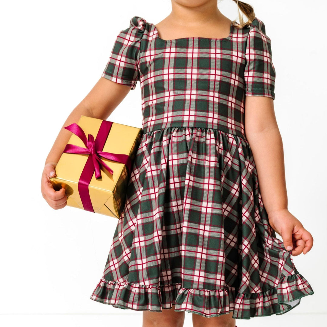 little girl holding Christmas gift in forest green and crimson plaid twirl dress with short puffed sleeves and square neck