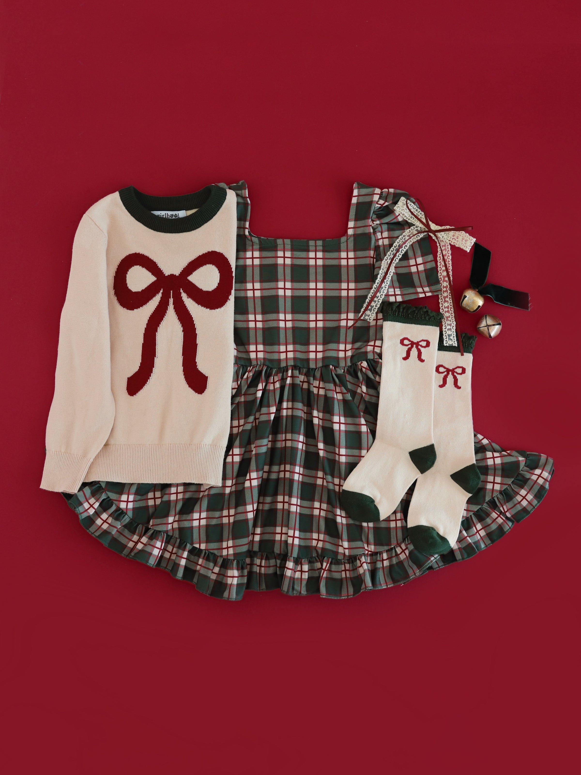 girls' Christmas outfit featuring forest green plaid twirl dress, cream knit sweater with crimson bow design and matching bow socks