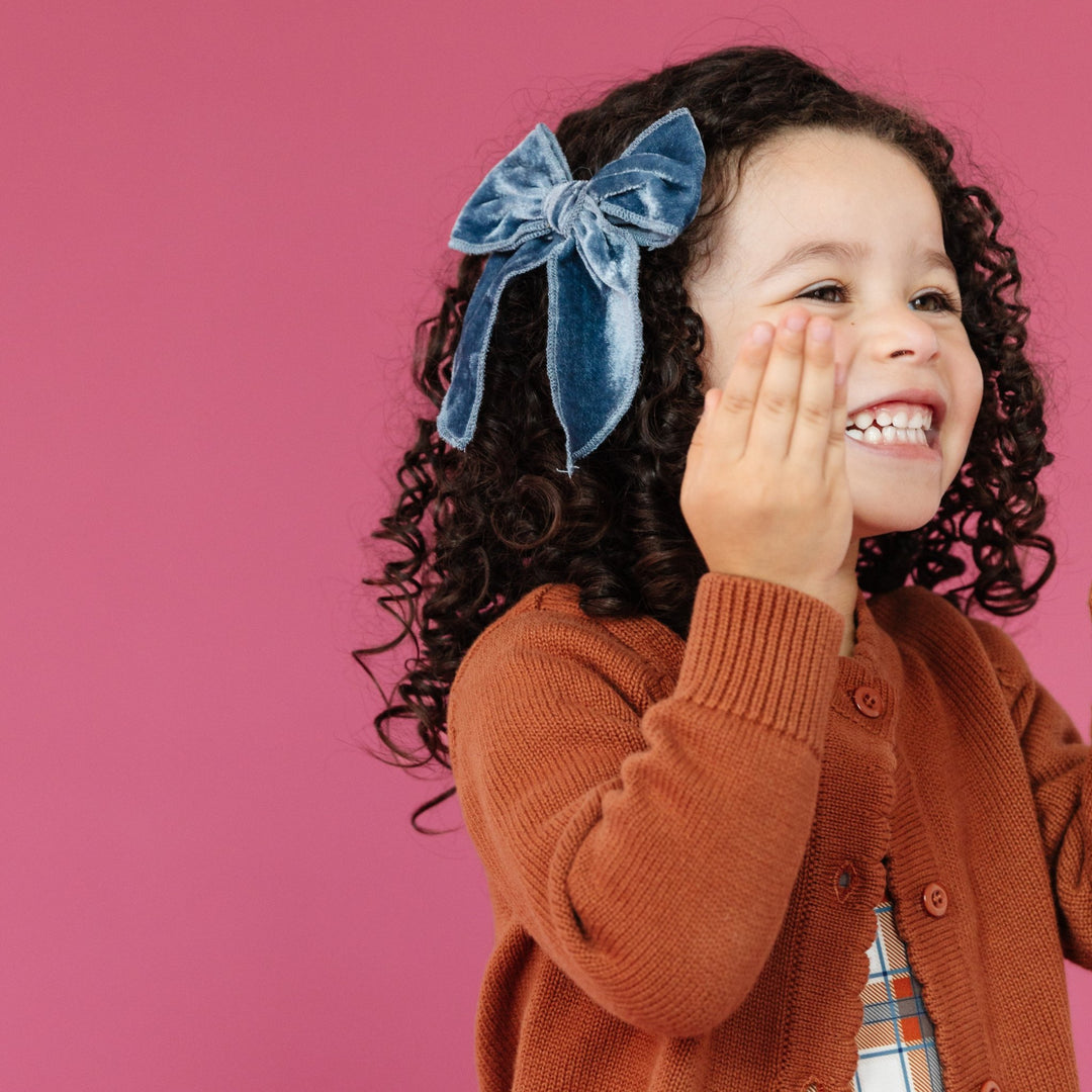 little girl in fall blue velvet hairbow on clip and brown knit cardigan buttoned over plaid dress 