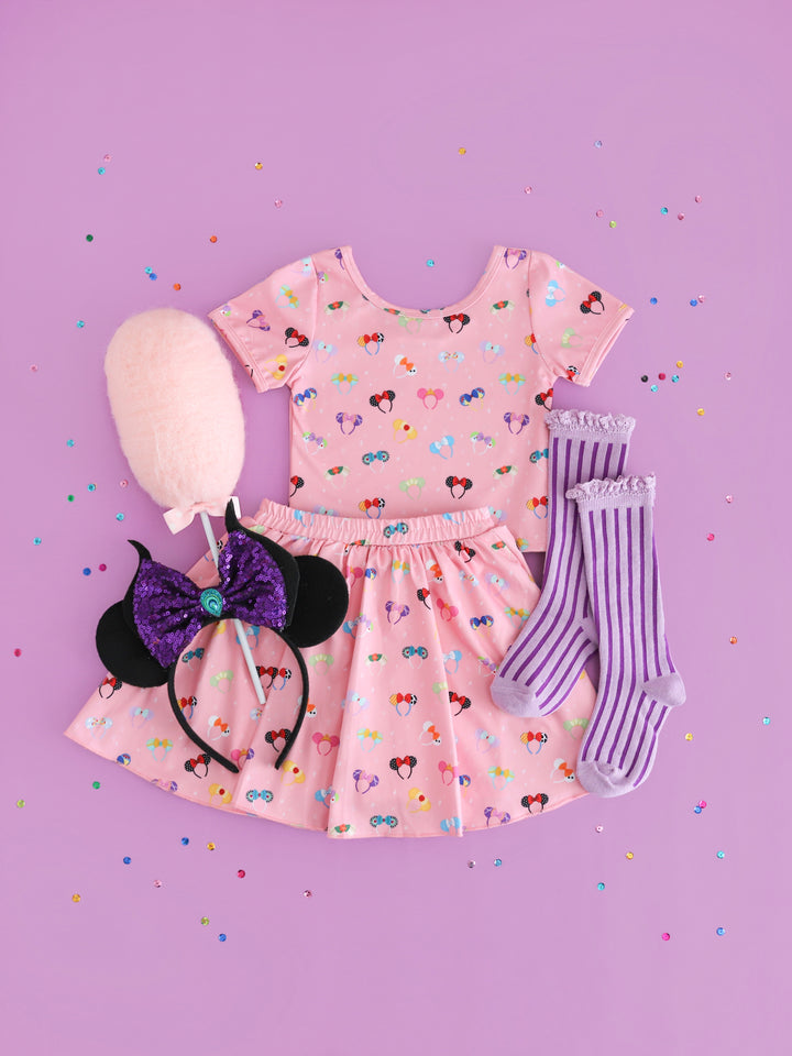 flatlay of girls disney outfit of matching pink shirt and skirt with character mickey ears and purple striped knee high socks with lace trim