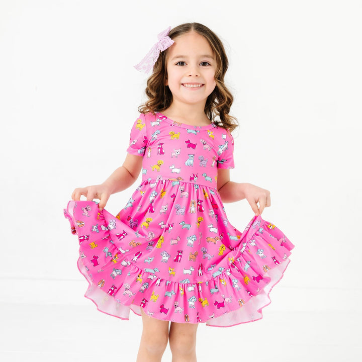 little girl in scoop neck twirl dress with colorful dogs on bright pink paired with lavender lace hair bow