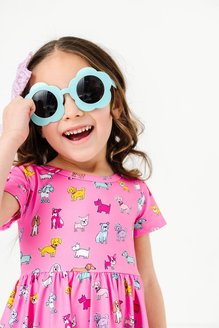 little girl in blue daisy sunglasses and pink twirl dress with colorful dog print
