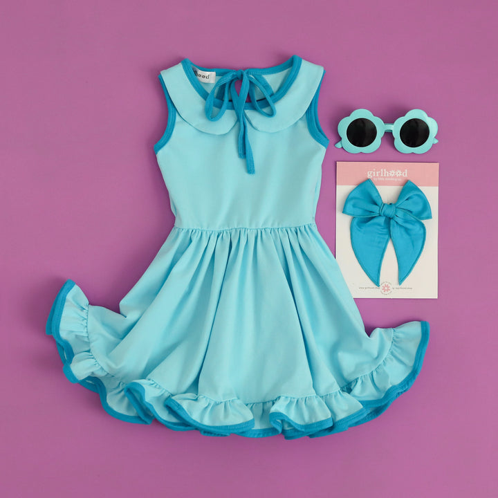 electric blue girls' cotton summer twirl dress with pockets and peter pan collar, styled with matching sunglasses and bright blue hair bow