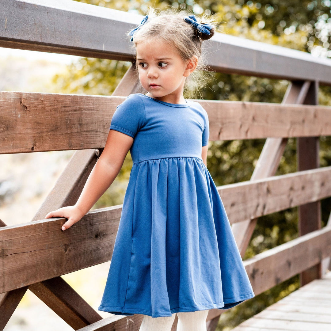 little girl with pigtail buns and blue velvet bows wearing denim blue cotton everyday pocket dress