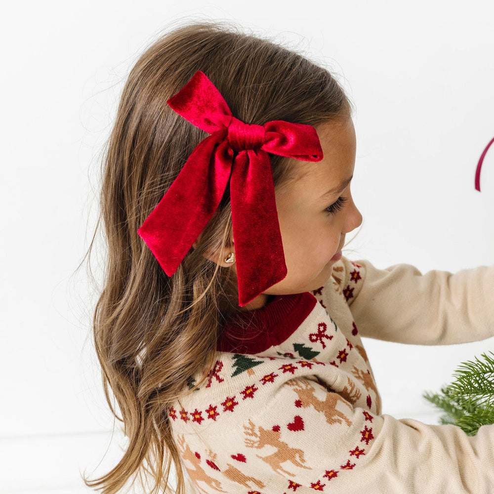 Child with red bow in hair decorating a Christmas tree.