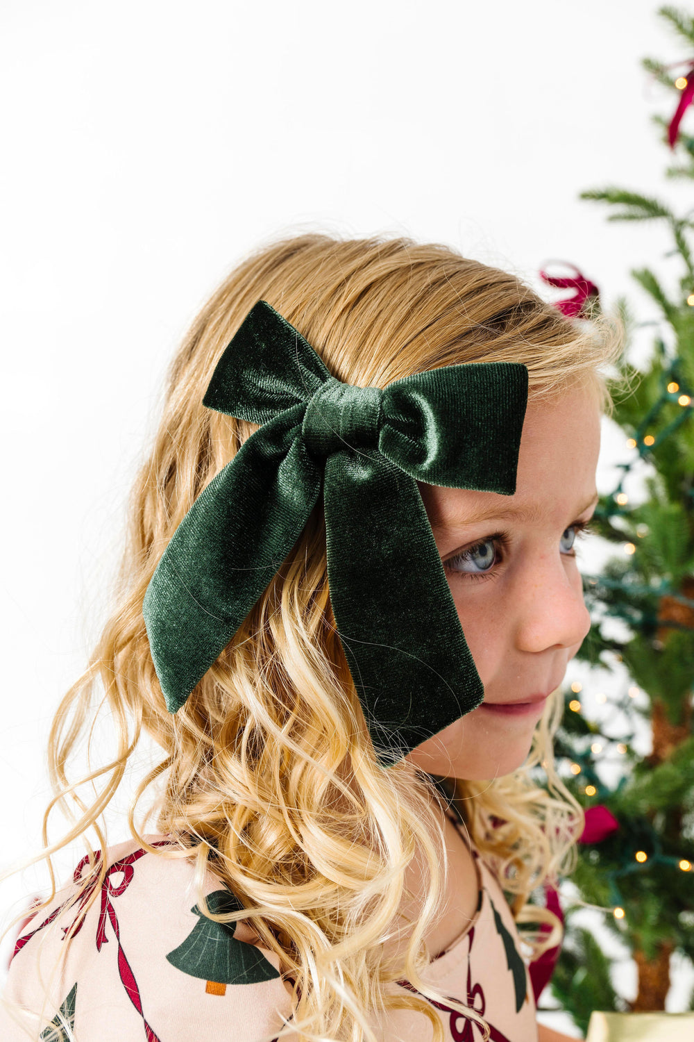 girl wearing a green velvet bow with a Christmas tree in the background