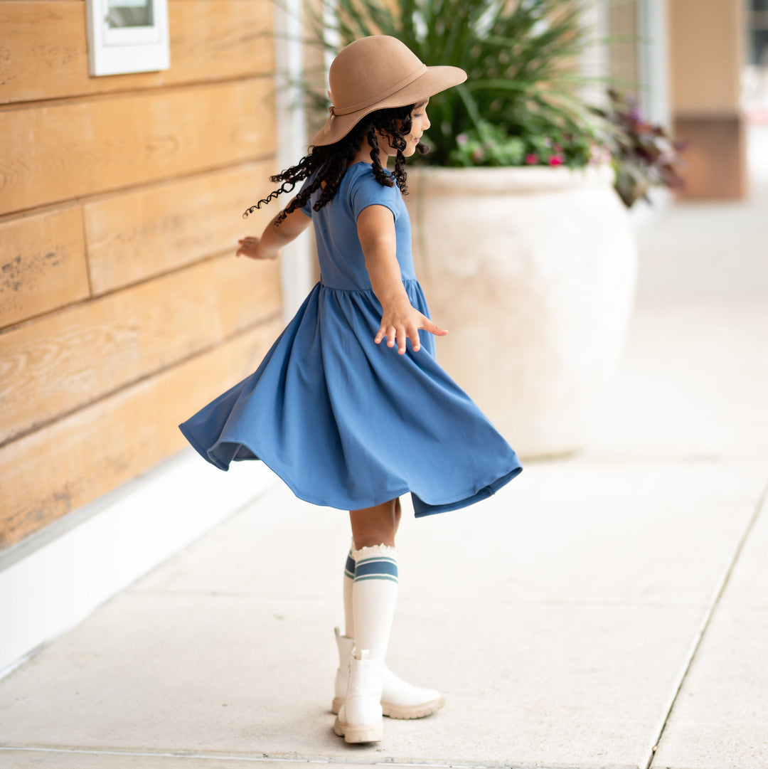 girl twirling in denim blue cotton dress and knee high socks