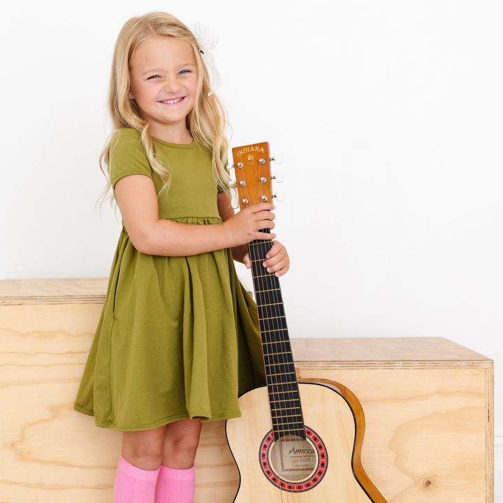 little girl holding guitar wearing bright olive green cotton pocket dress and cute pink knee high socks