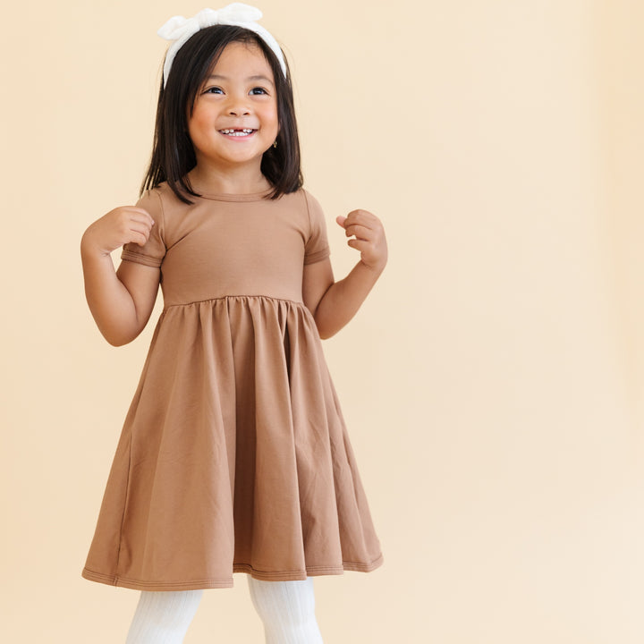 little girl wearing neutral toned mocha everyday cotton dress with pockets.