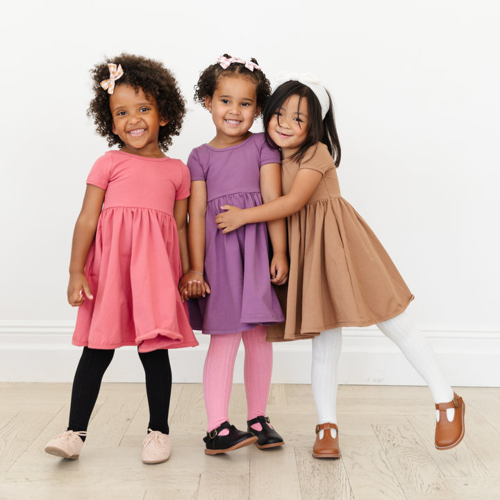 three little girls wearing cotton everyday pocket dresses in old rose pink, plum purple and neutral mocha.