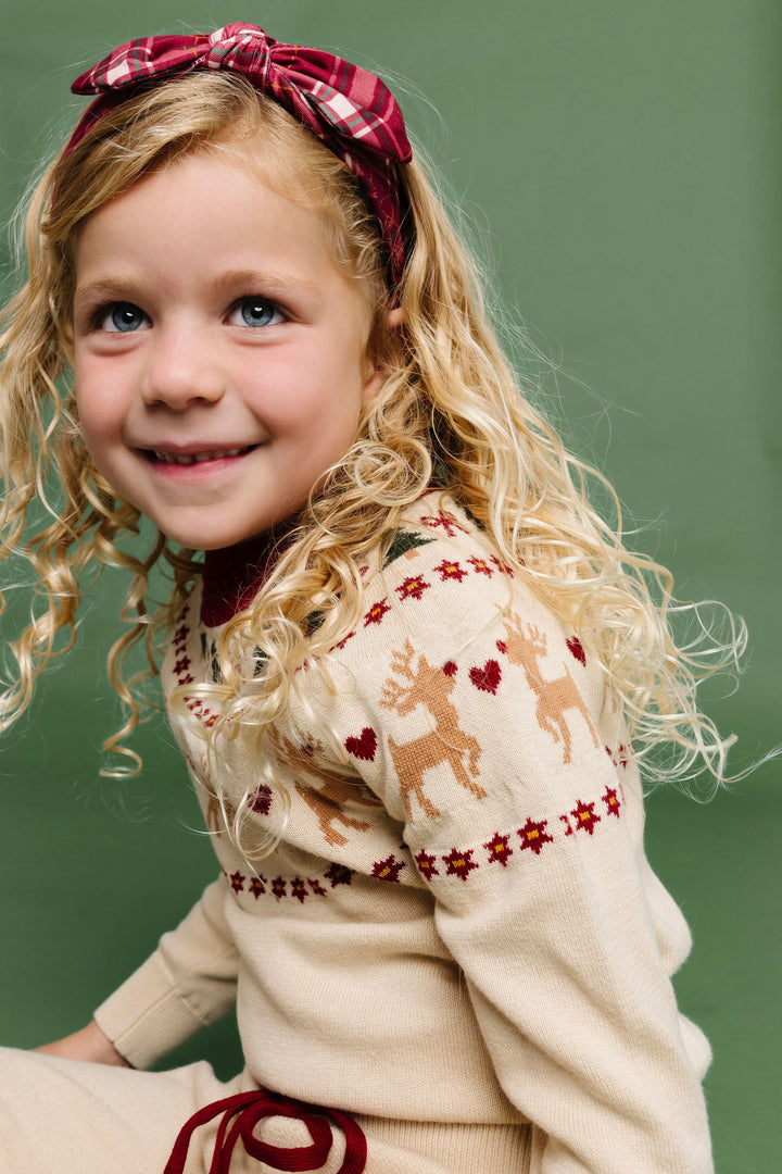 little girl in reindeer themed faire isle cream sweater with matching crimson plaid bow headband for Christmas