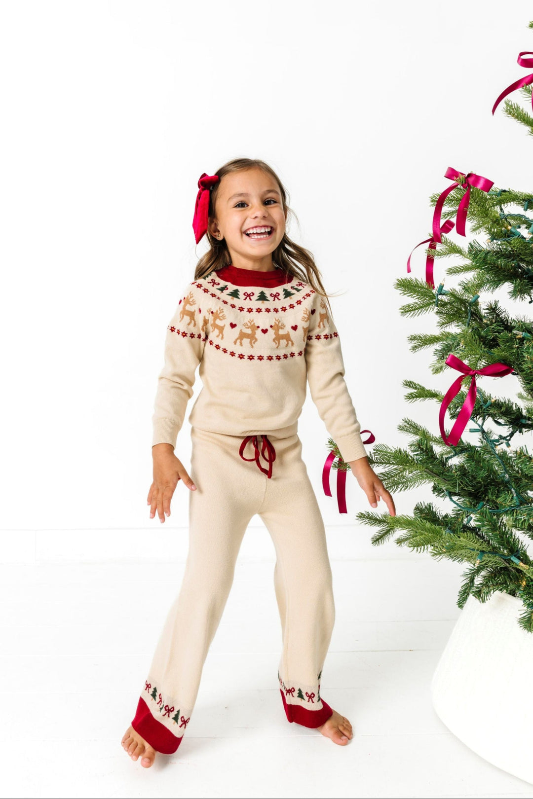 young girl by Christmas tree in pullover sweater and pant set with cream base and crimson and forest green fair isle print for Christmas