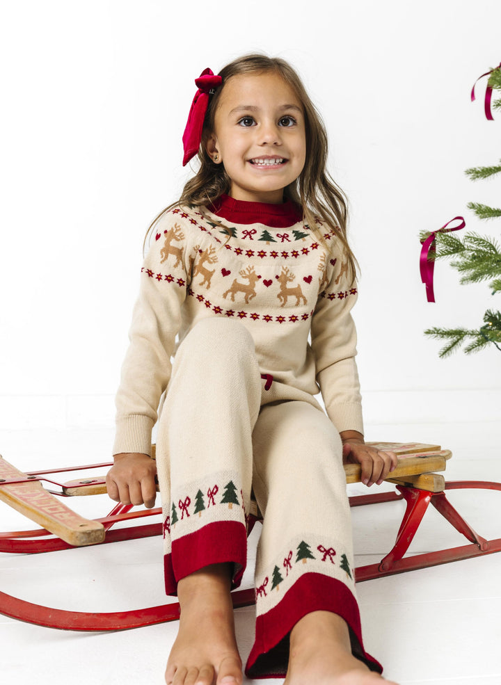 little girl sitting on sled in Christmas themed fair isle print cream pullover sweater and matching sweater pants