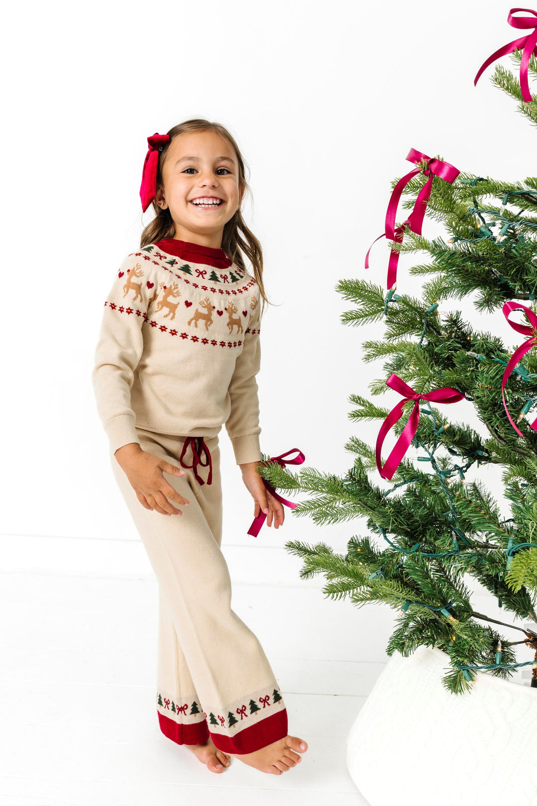 young girl by Christmas tree in pullover sweater and pant set with cream base and crimson and forest green fair isle print for Christmas