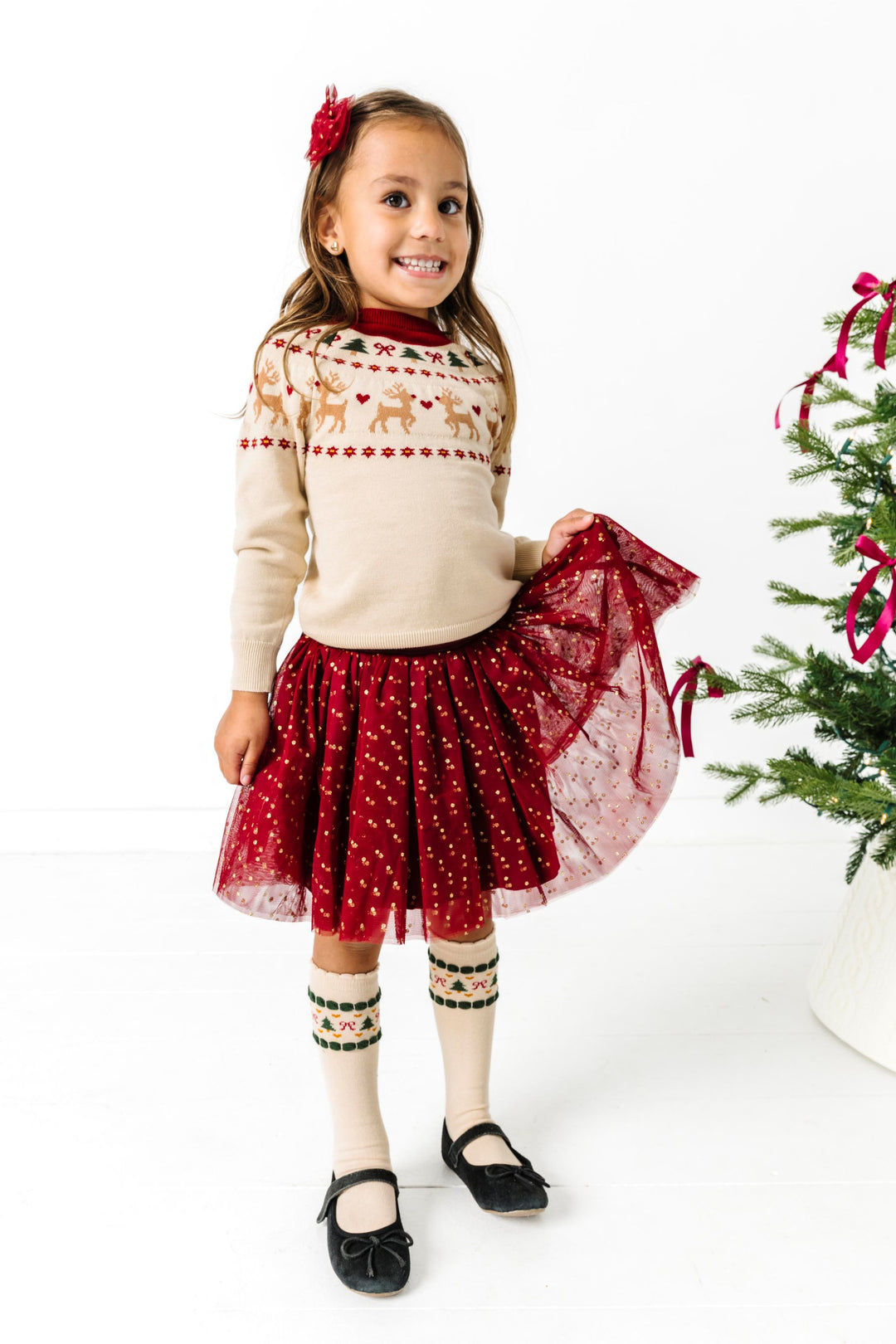 little girl in fair isle Christmas outfit with matching cream sweater and socks, crimson tulle skirt with gold sparkly dots and matching tutu bow