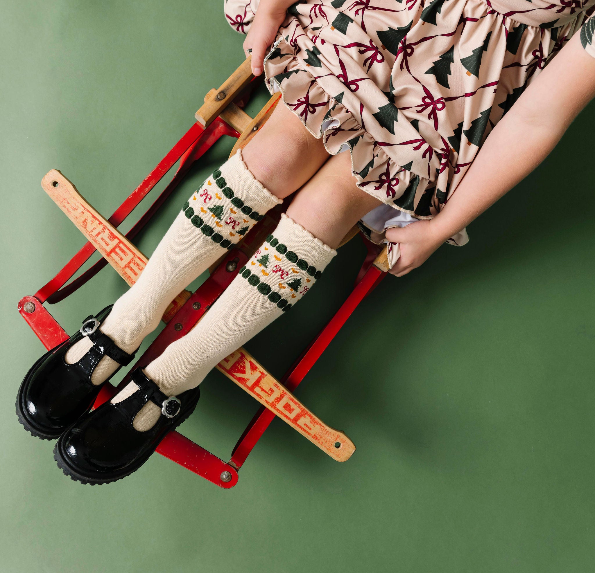 little girl on sled with cream scalloped knee-high socks with faire-isle design at the calf and matching Christmas tree dress