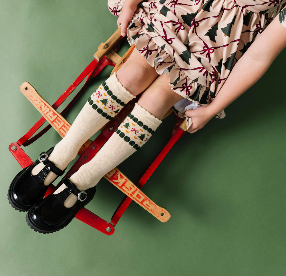 little girl on sled with cream scalloped knee-high socks with faire-isle design at the calf and matching Christmas tree dress
