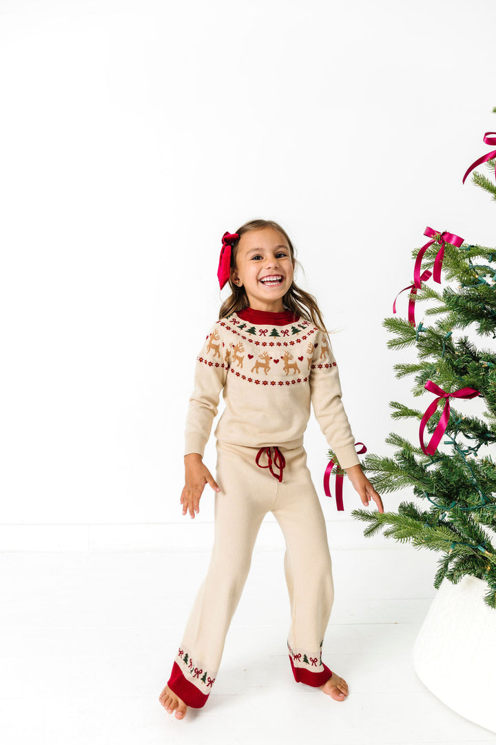 little girl by Christmas tree in cream pullover sweater and sweater pant set with fair isle reindeer print