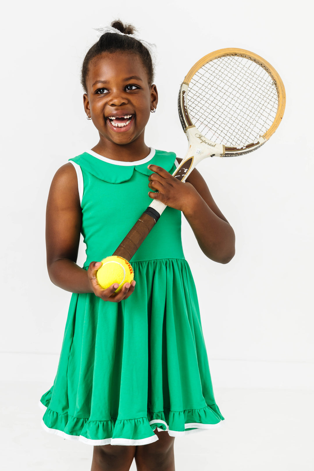 little girl in grass green sleeveless twirl dress with peter pan collar holding tennis ball and racket