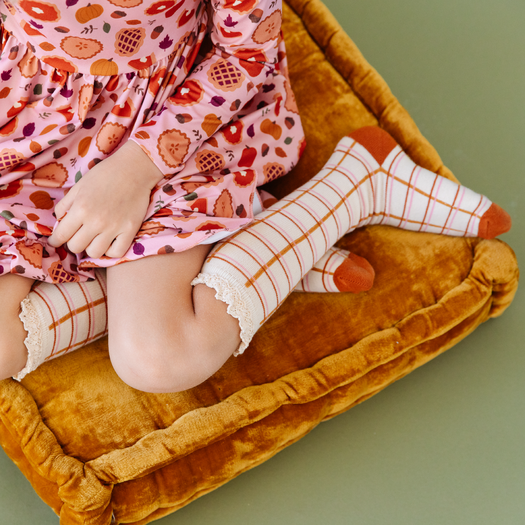 girl with harvest fall grid knee highs and pumpkin pie dress sitting on yellow floor cushion