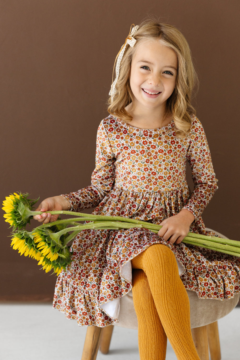 little girl holding sunflowers in long sleeve velvet floral twirl dress with matching mustard cable knit tights and lace bow for fall