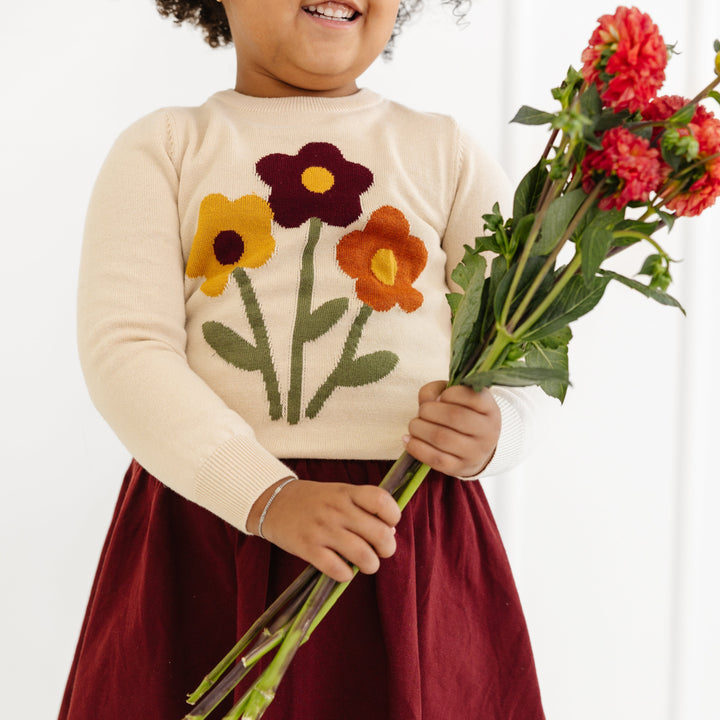 closeup of little girl with flowers wearing cream floral sweater and matchihng burgundy skort for fall family photos