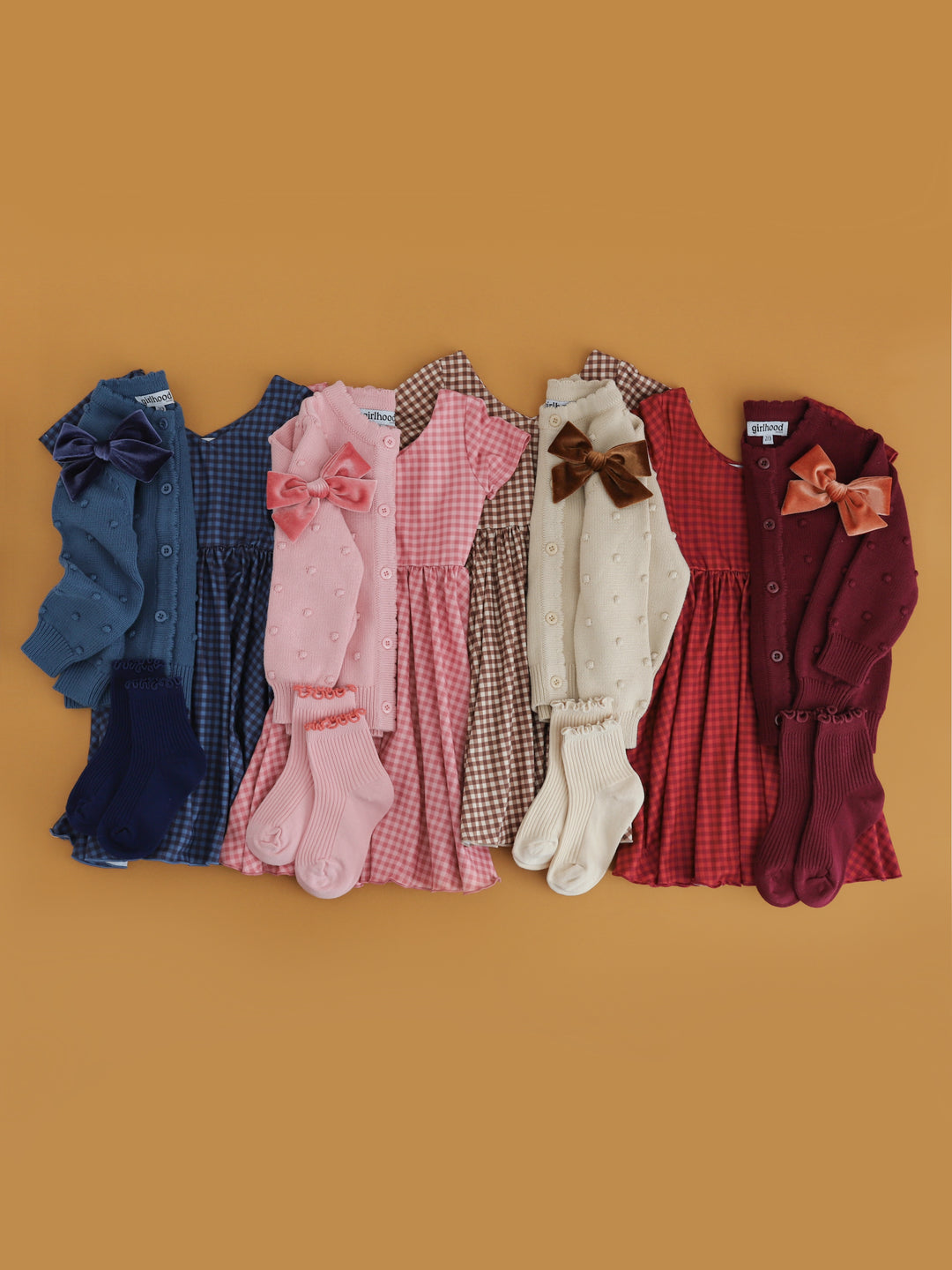 flat lay of four fall gingham twirl dresses and matching cardigans, velvet bows and midi socks