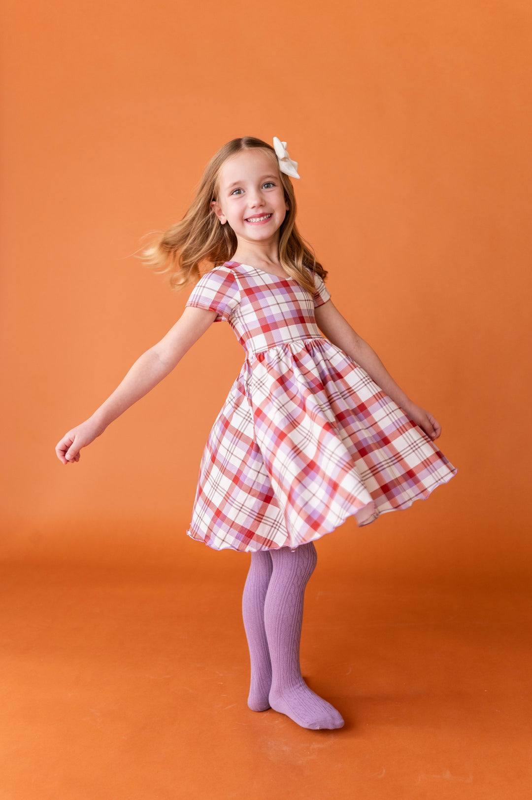 young girl twirling in ivory, rust and amethyst v-neck twirl dress with lettuce trim paired with matching amethyst tights