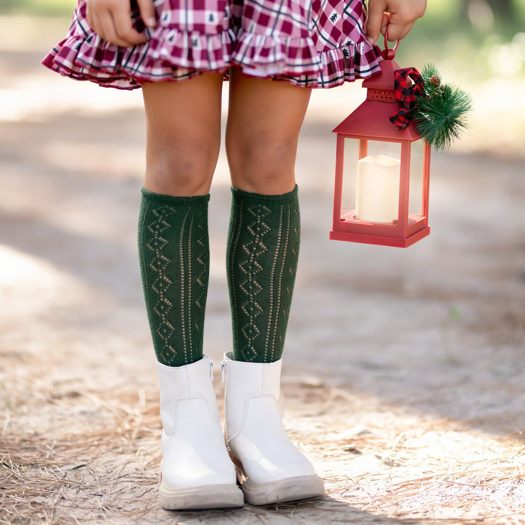 girl in christmas outfit holding lantern with open crochet forest green knee highs