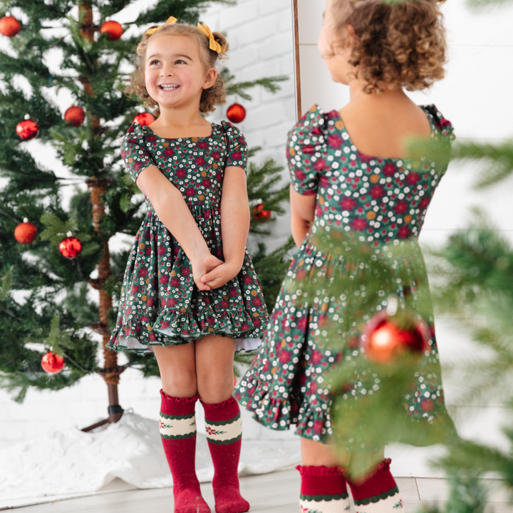 little girl looking in the mirror in poinsettia print holiday dress and matching Christmas socks