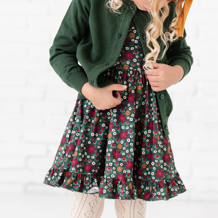 little girl in poinsettia Christmas dress, matching forest green cardigan and vanilla pointelle tights