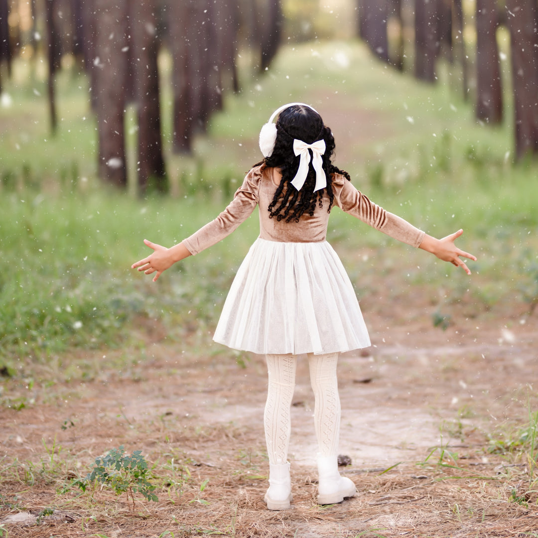 little girl twirling in gold velvet party dress with sparkly cream tulle skirt during snowfall