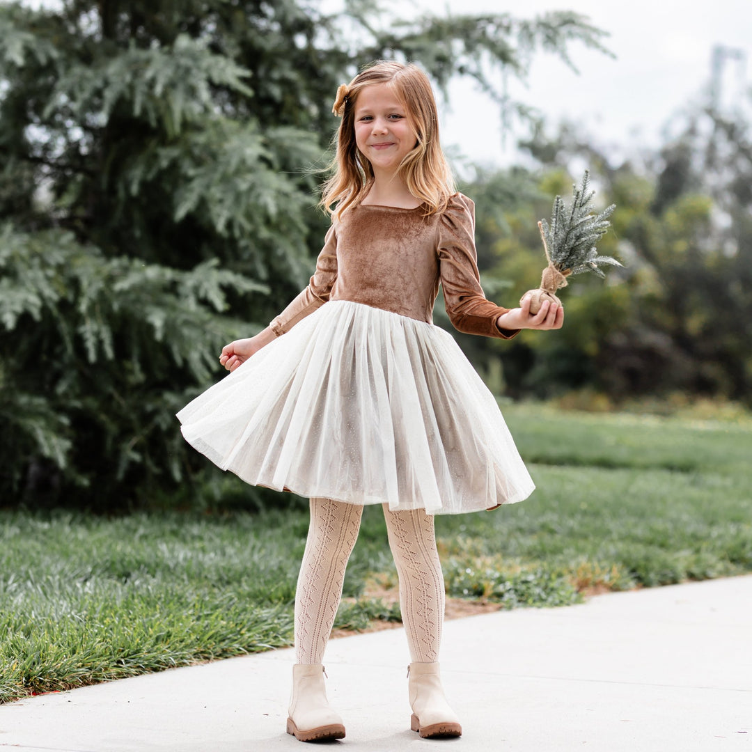 little girl at tree farm with gold velvet and tulle holiday dress and cream tights with open knit design