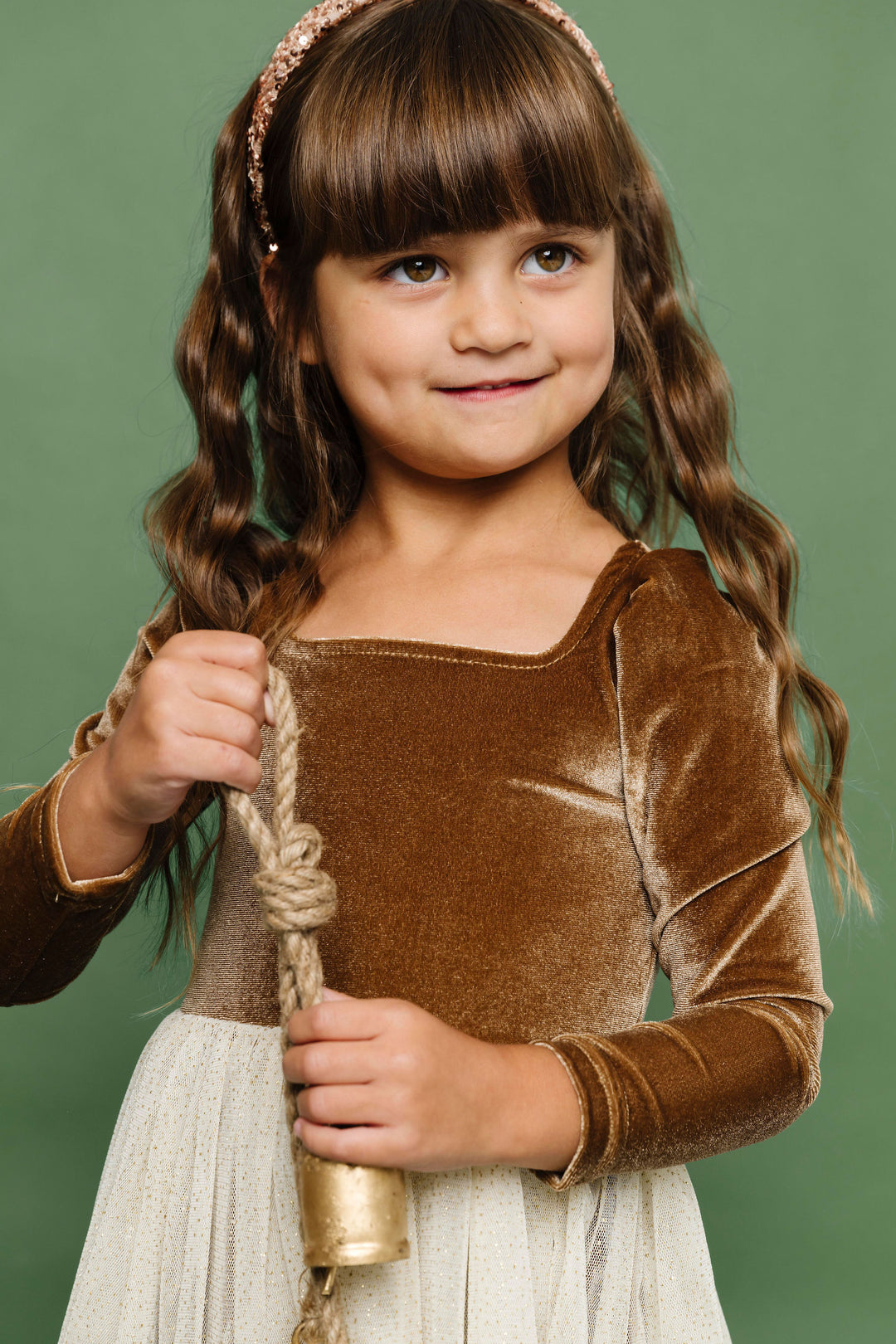 little girl holding Christmas bell in golden brown velvet tutu dress and gold sequin headband
