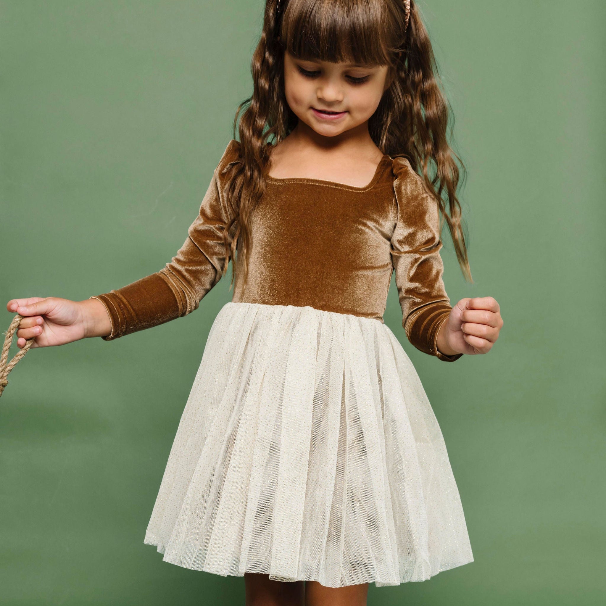 little girl in fancy velvet and tulle Christmas dress in shades of golden brown and cream paired with Christmas tree print knee socks and gold sparkle headband