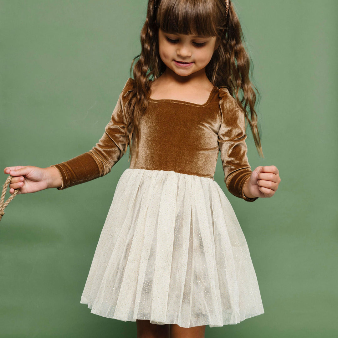 little girl in fancy velvet and tulle Christmas dress in shades of golden brown and cream paired with Christmas tree print knee socks and gold sparkle headband