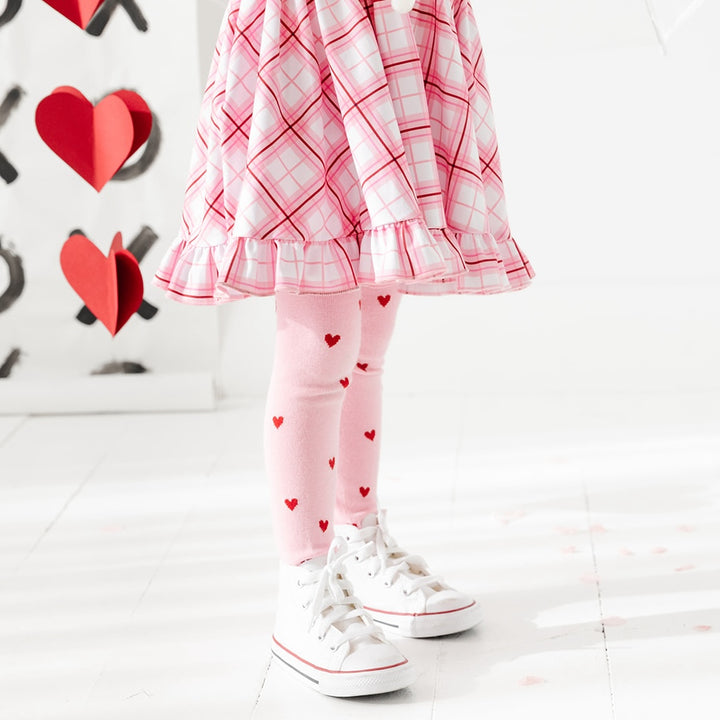 little girl standing in valentines plaid dress and matching pink and red heart tights