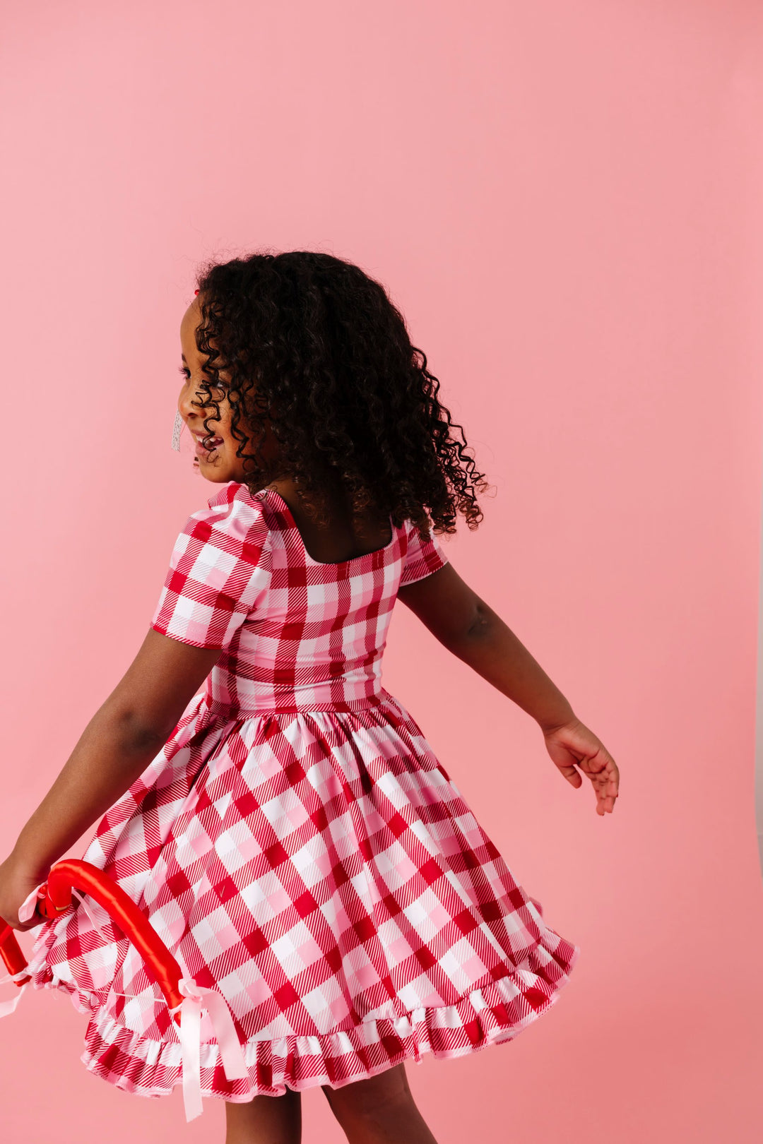young girl twirling in pink, red and white plaid short sleeve twirl dress holding cupids bow