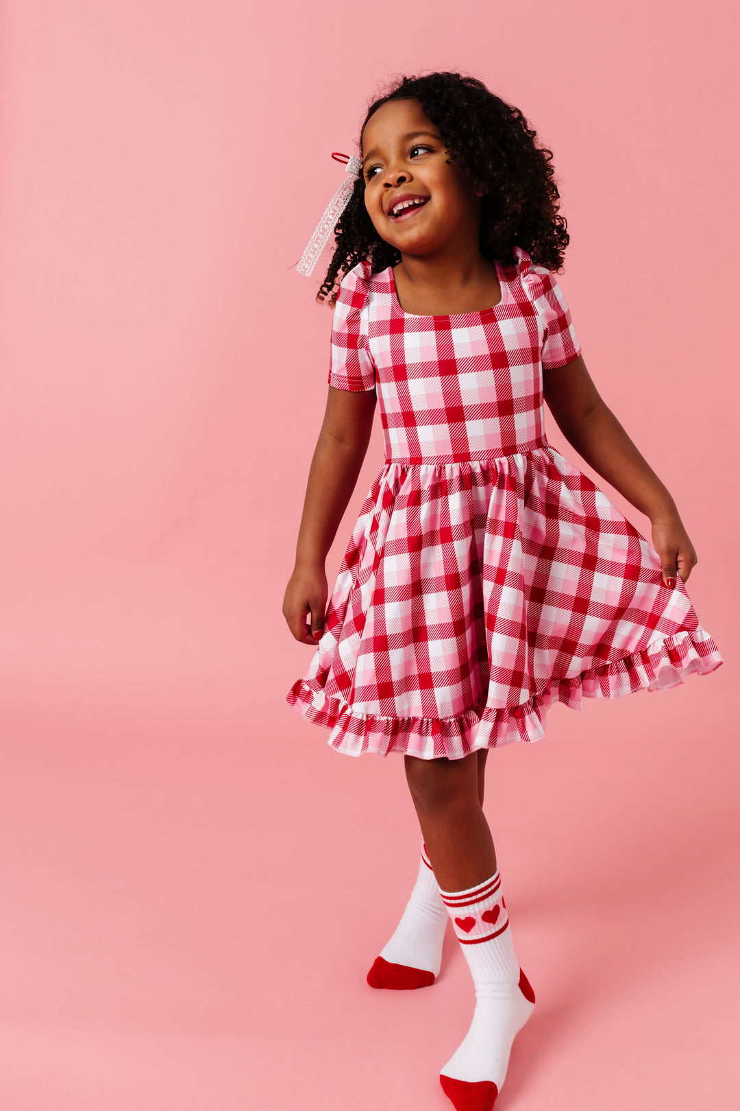 young girl in valentines inspired plaid square neck twirl dress, lace ribbon hair bow and valentines themed athletic ankle socks