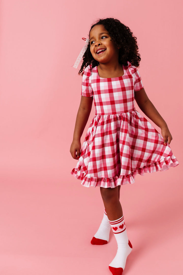 young girl in valentines inspired plaid square neck twirl dress, lace ribbon hair bow and valentines themed athletic ankle socks