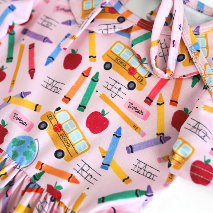 closeup of back to school print twirl dress bodice featuring yellow school busses, apples, crayons and pencils